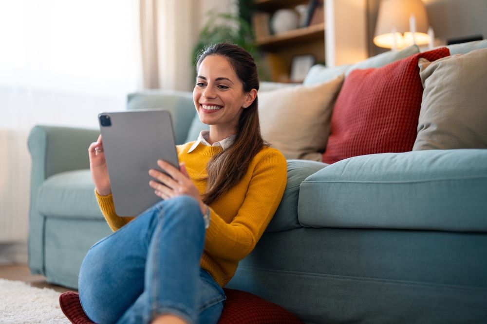 A,Cheerful,Woman,Sits,Comfortably,On,The,Floor,,Tablet,In